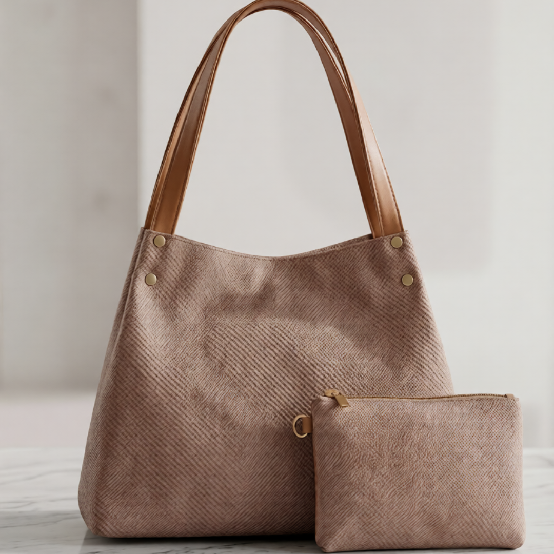 A herringbone-patterned taupe tote bag with tan leather shoulder straps and a matching zippered pouch, displayed on a white marble surface against a neutral light gray background.